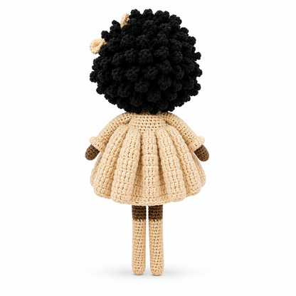 Crocheted doll with black hair and a beige dress on a white background